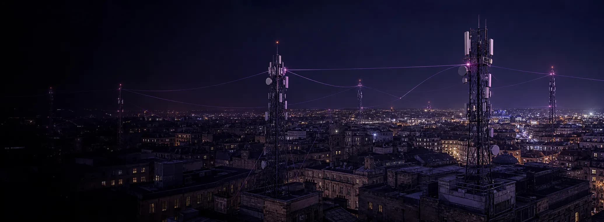 A city at night from rooftop height, two tall lattice telecoms masts standing close in the foreground with their antenna panels and dishes lit, more masts further off, and fine violet lines of light arcing between them across the city.