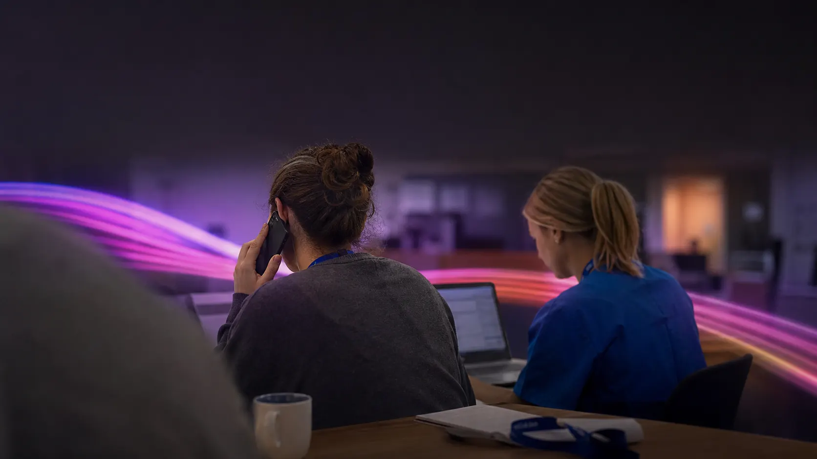 Two health centre staff at a shared desk, one taking a call on a mobile