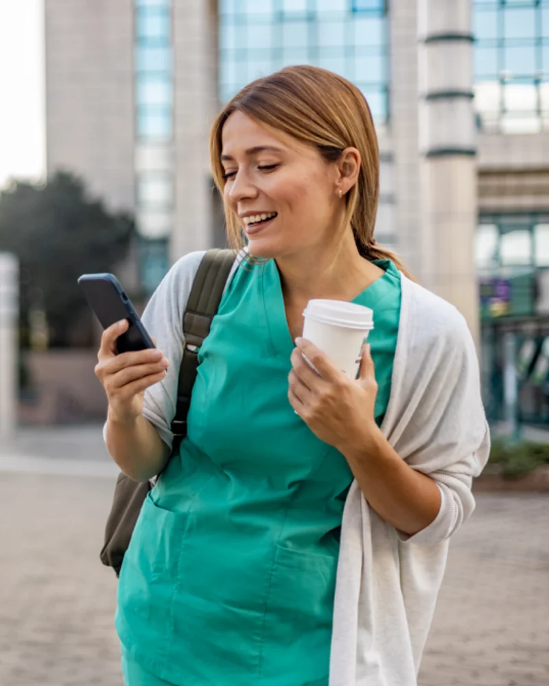 A nurse checking her mobile phone outside a healthcare building